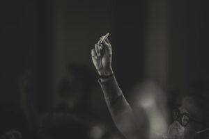 A thoughtful hand gesture by a masked person in a dimly lit setting, emphasizing contemplation.